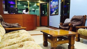 A hotel lobby with a reception desk, a sofa, a wooden coffee table, and leather armchairs. - Babblers Park (Migori)