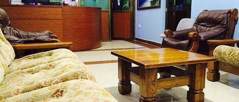 Un vestíbulo de hotel con mostrador de recepción, un sofá, una mesa de centro de madera y sillones de cuero.