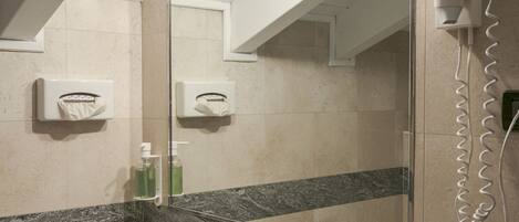 Un baño con un lavabo blanco, un espejo, un secador de pelo y un dispensador de jabón.