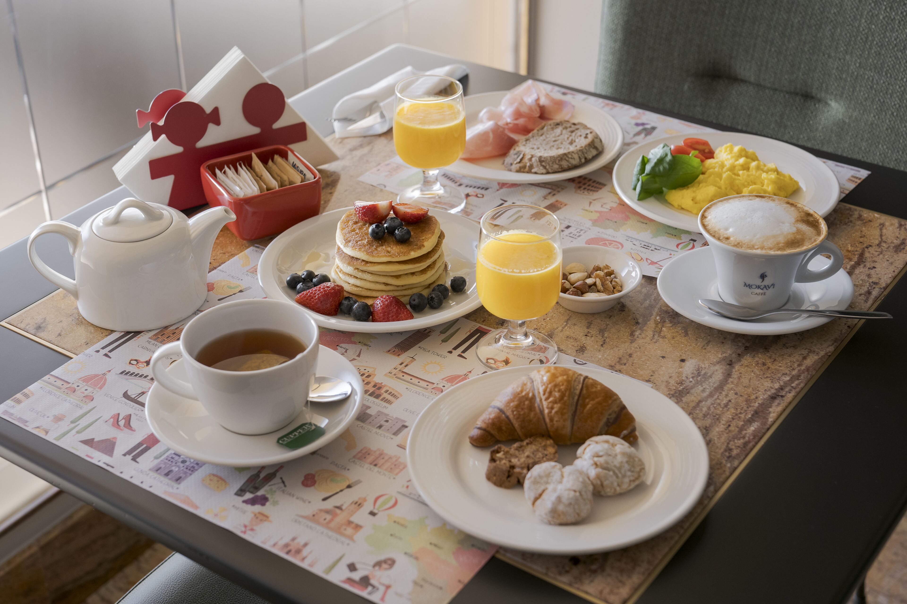 A breakfast table with a croissant, coffee, juice, and a plate of scrambled eggs and toast.