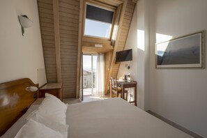 A bedroom with a large bed, a desk with a chair, a TV mounted on the wall, and a window with a view of the outside.