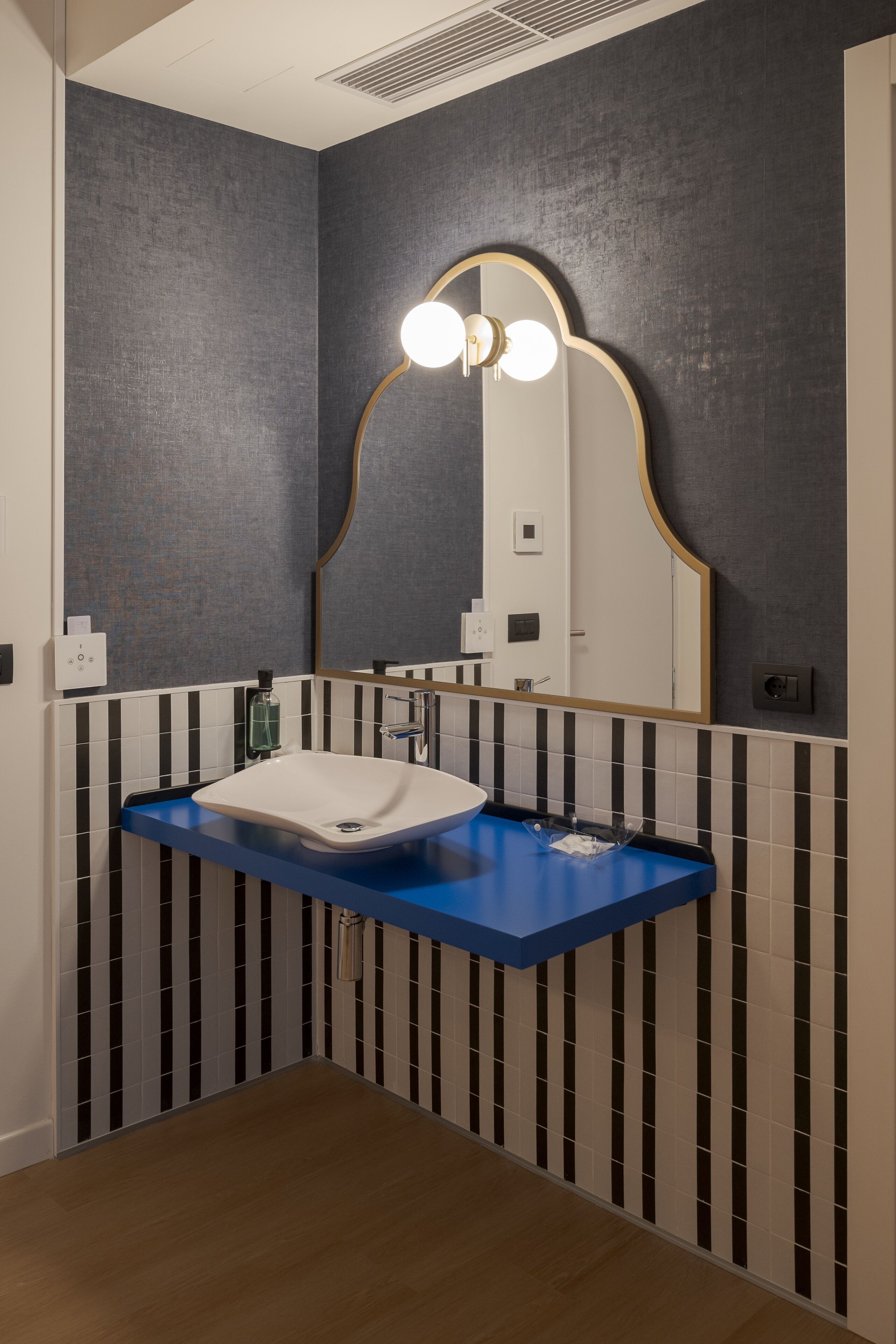 A bathroom with a white sink, blue countertop, and a large mirror with a gold frame.