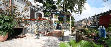 An outdoor courtyard with a tiled floor, a decorative metal fence, and potted plants.