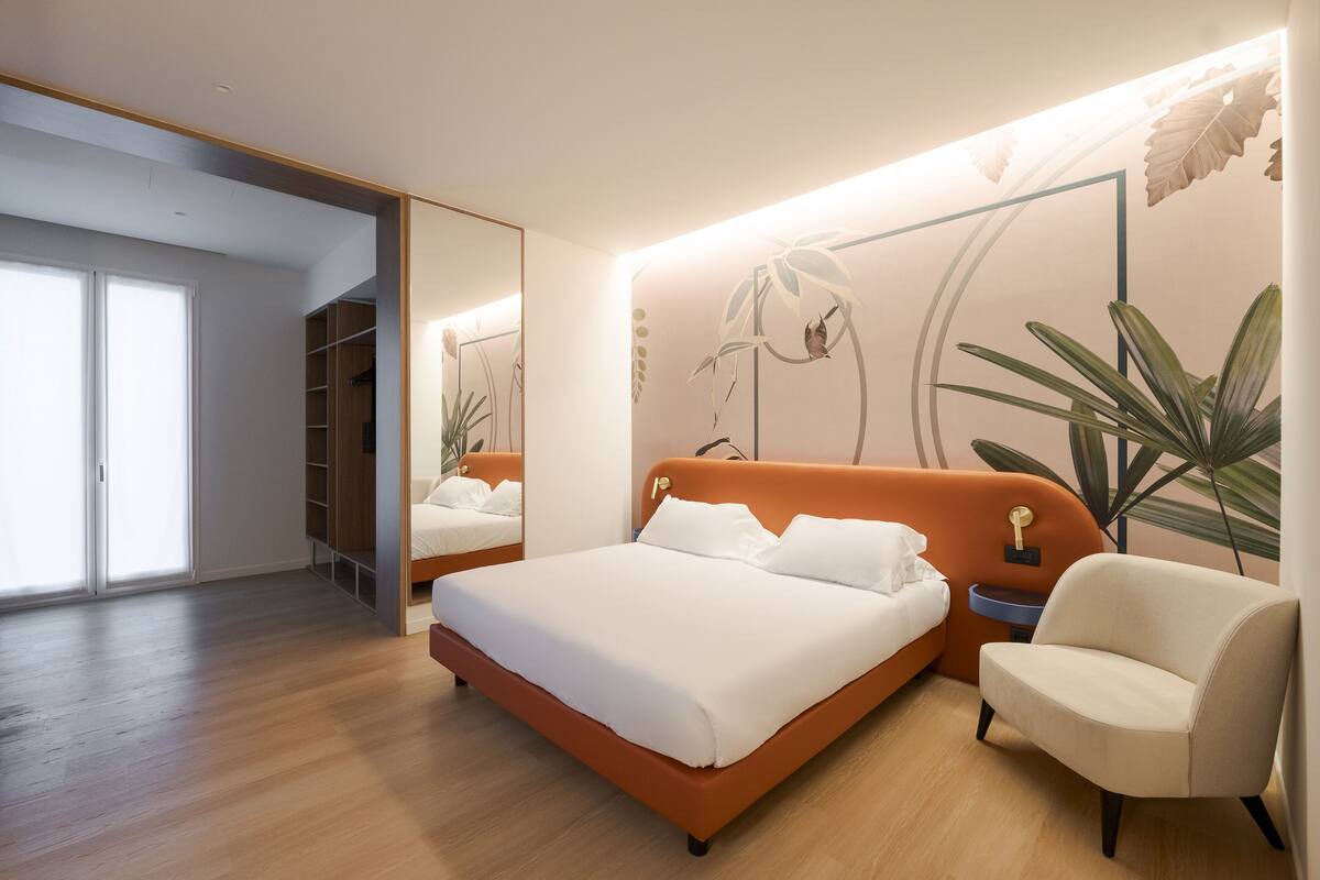 A modern bedroom with a large bed, a chair, a bedside table, and a wardrobe.