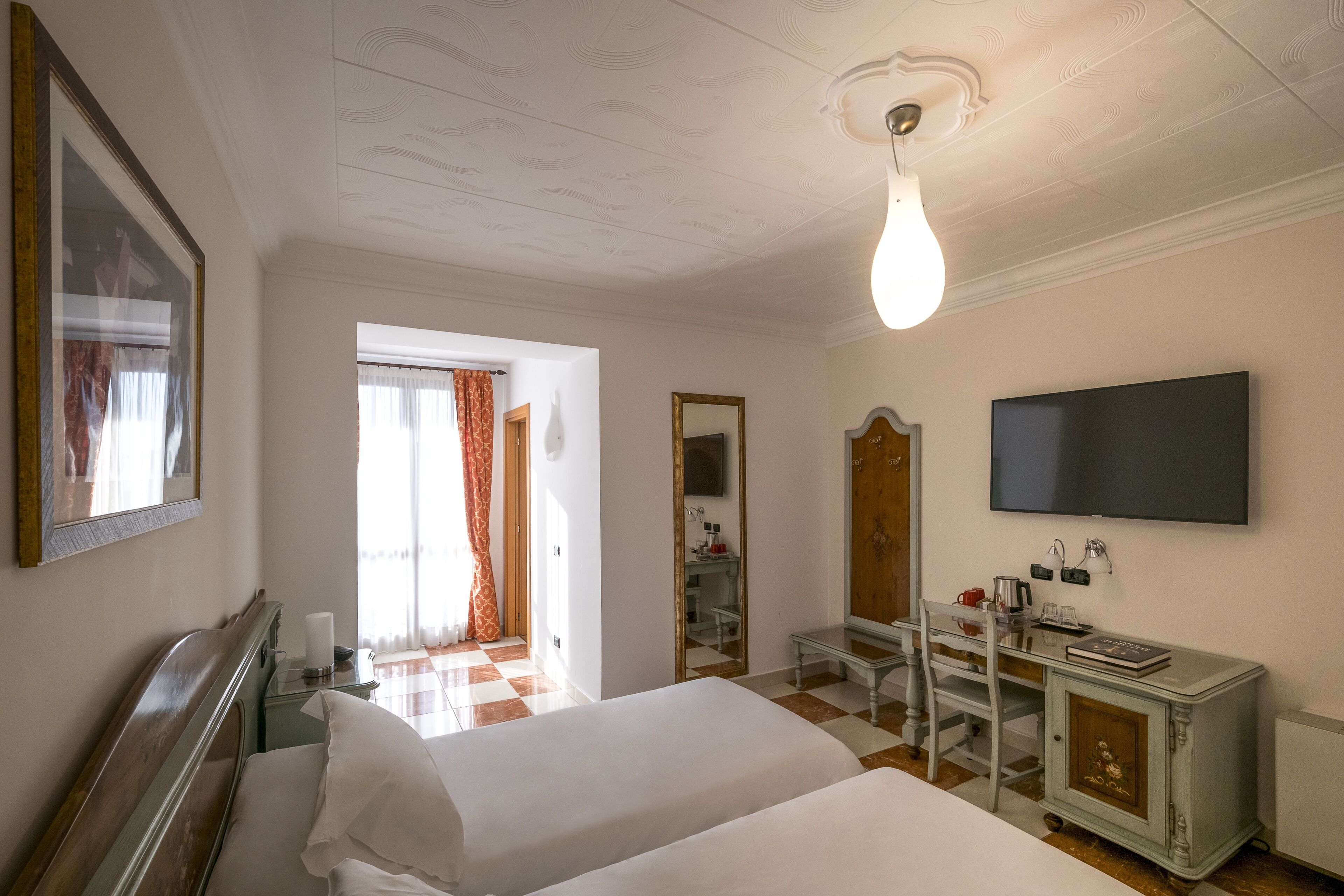 Hotellihuone, jossa on sänky, työpöytä, peili, televisio ja vaatekaappi.