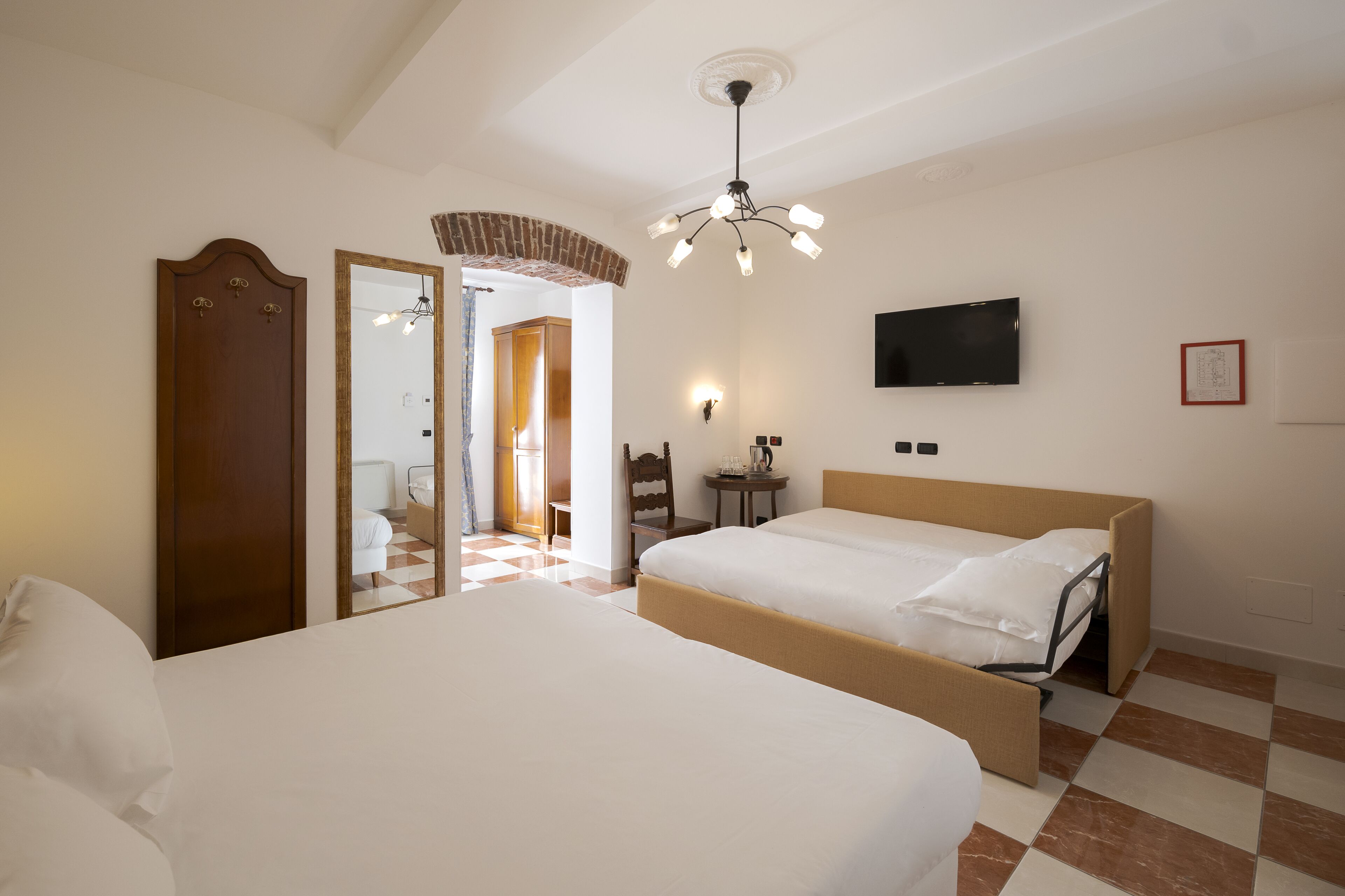 Een hotelkamer met twee bedden, een televisie, een spiegel en een deur naar een andere kamer.