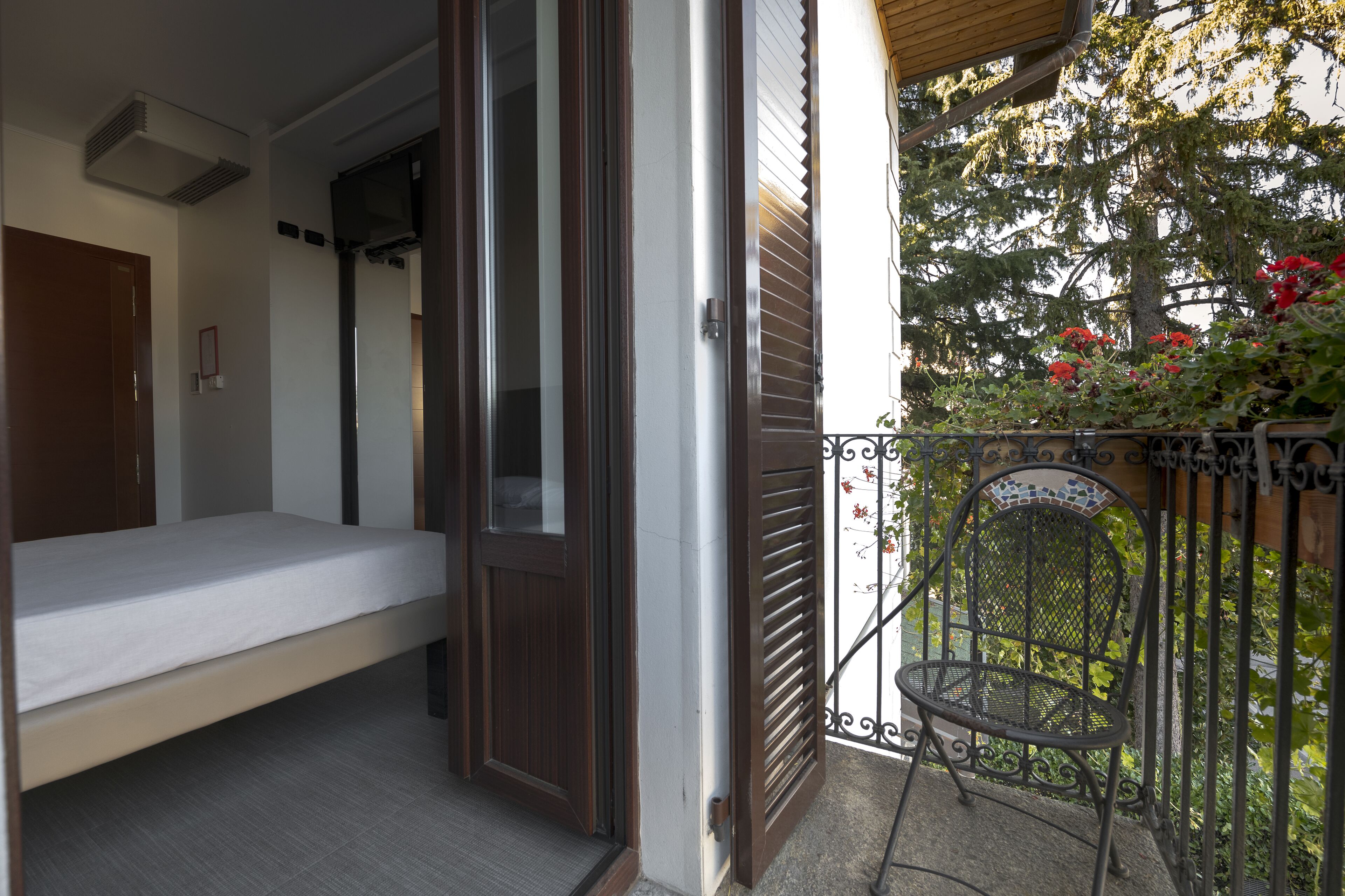 A balcony with a bed, a chair, and a view of trees and flowers.