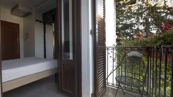 Un balcón con una cama, una silla y vistas a árboles y flores.