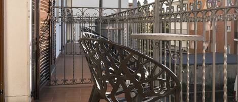 A balcony with a metal chair, a tiled floor, and a metal railing.