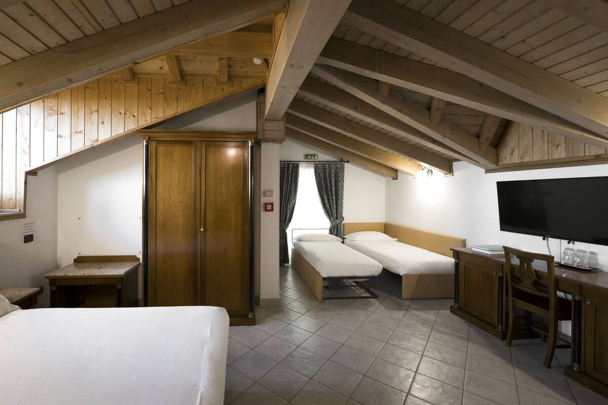 A room with a wooden ceiling, a bed, a desk, a TV, and a door.