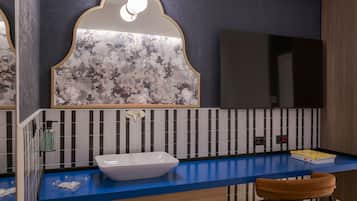 A bathroom with a white sink, blue countertop, striped wall tiles, a mirror with floral design, and a towel rack.