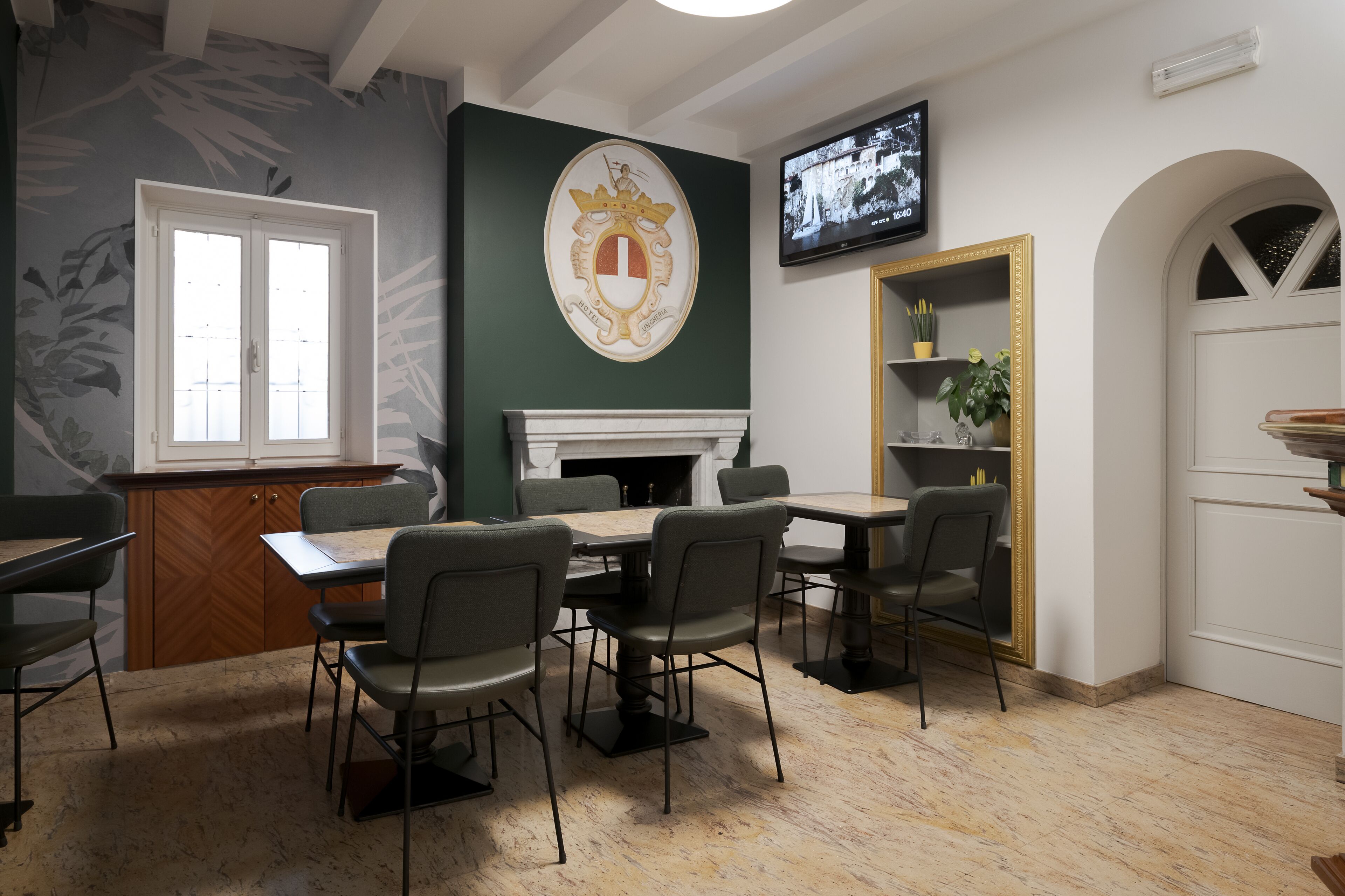 A dining area with a fireplace, a television mounted on the wall, and a green accent wall with a coat of arms.