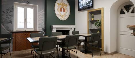 A dining area with a fireplace, a television mounted on the wall, and a green accent wall with a coat of arms.