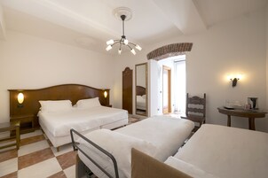Habitación de hotel con dos camas, cabecera de madera, una mesita con lámpara, espejo y aplique de pared.