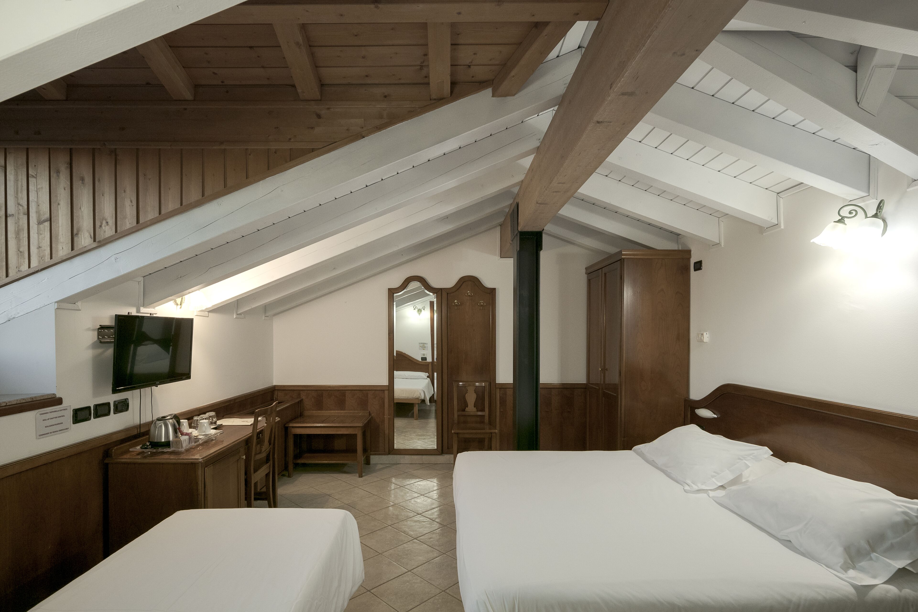 A hotel room with two beds, a desk, a chair, a television, and a mirror.