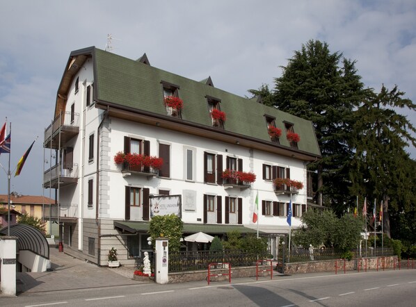 A multi-story hotel with balconies adorned with red flowers, a sign indicating it is a hotel, and flags on the building. - Hotel Ungheria Varese 1946 (Varese)