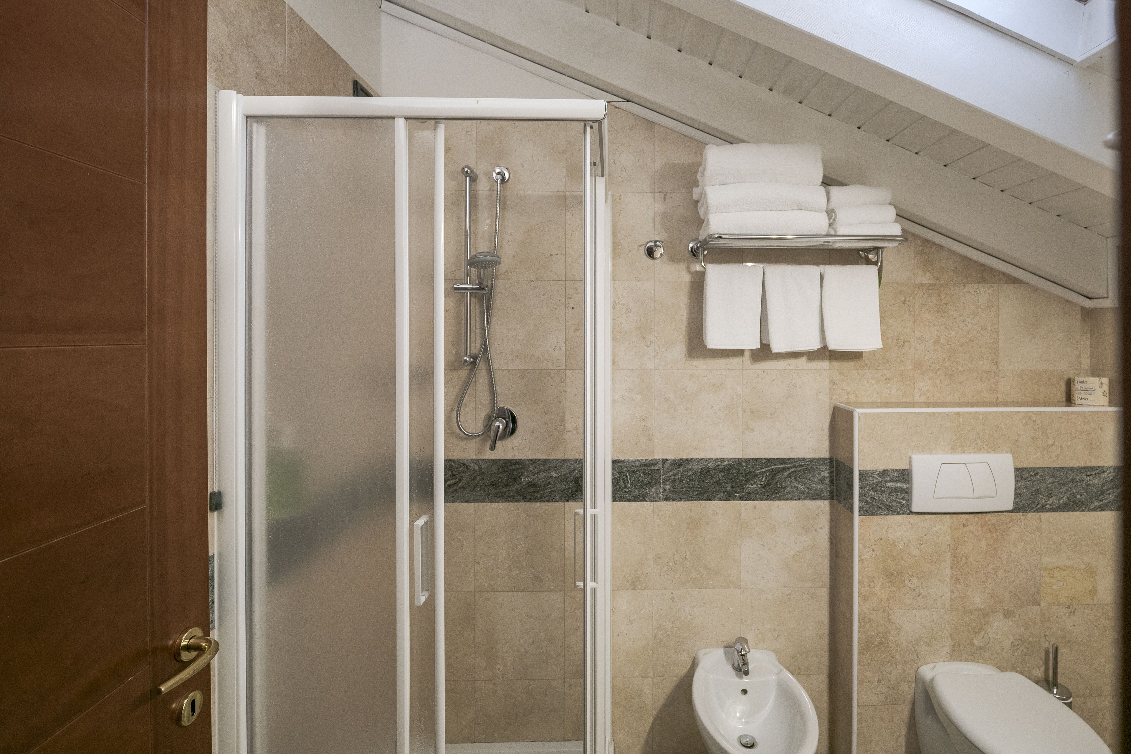 A hotel bathroom with a glass-enclosed shower, a sink, a toilet, and a towel rack with folded towels.
