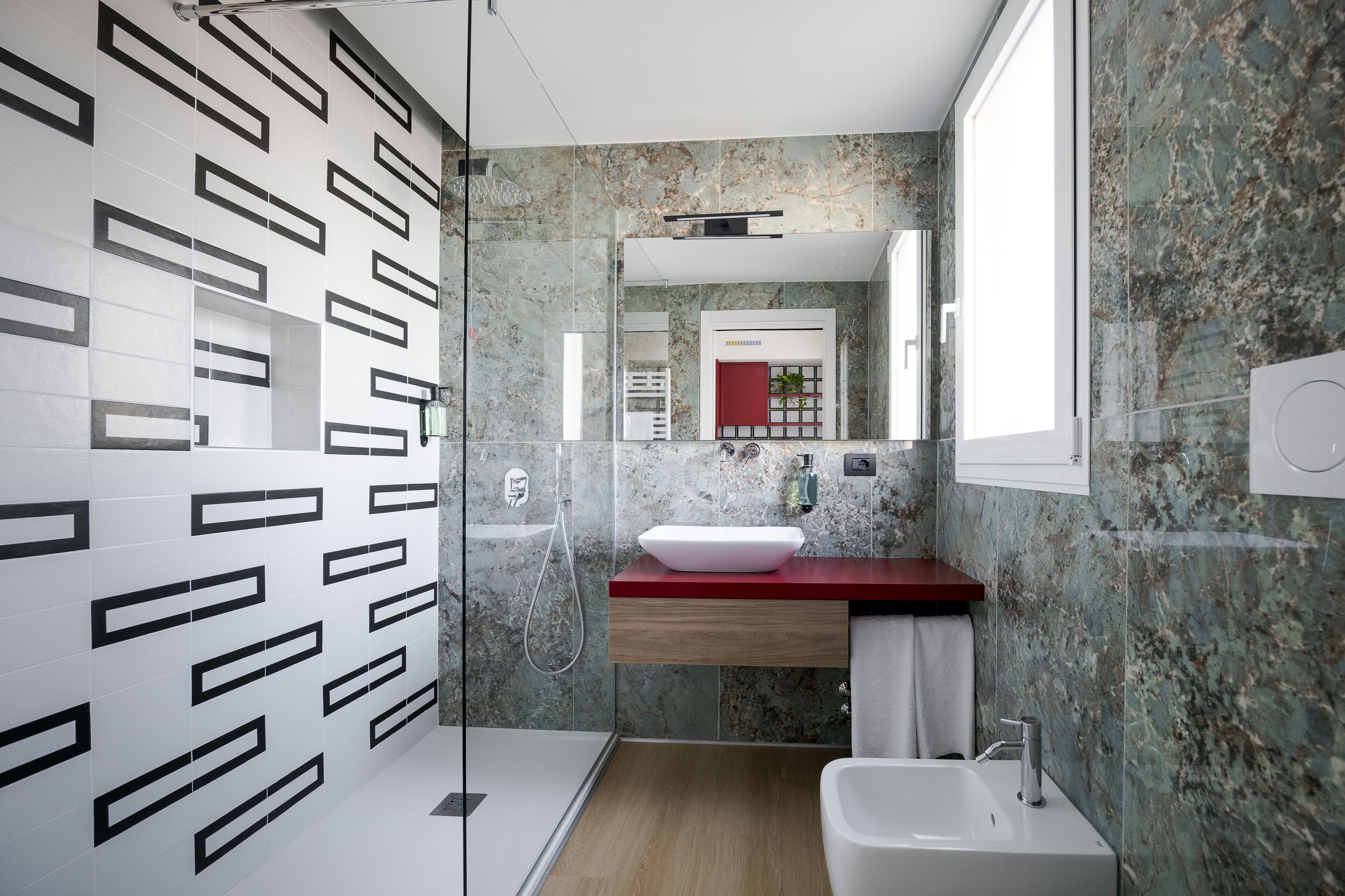 Un baño moderno con cabina de ducha de vidrio, un lavabo blanco y un salpicadero de mármol.