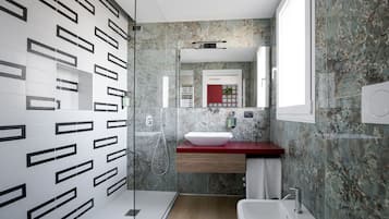 Un baño moderno con cabina de ducha de vidrio, un lavabo blanco y un salpicadero de mármol.