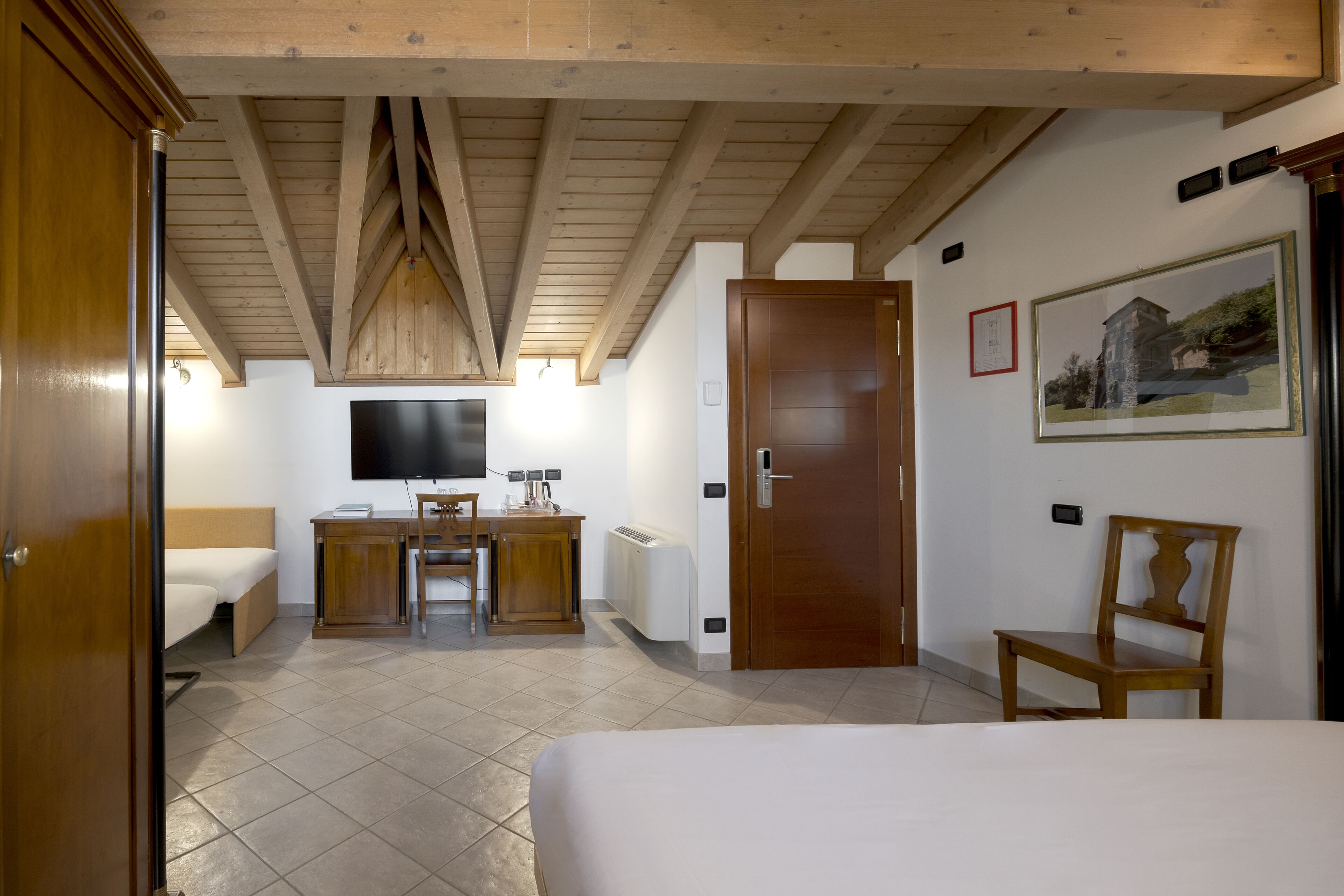 A hotel room with a bed, a desk, a chair, a TV, and a door.