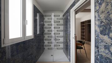 A modern bathroom with a glass shower enclosure, a wooden floor, and a built-in shelving unit.