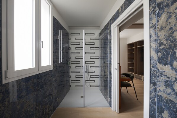 A modern bathroom with a glass shower enclosure, a wooden floor, and a built-in shelving unit.