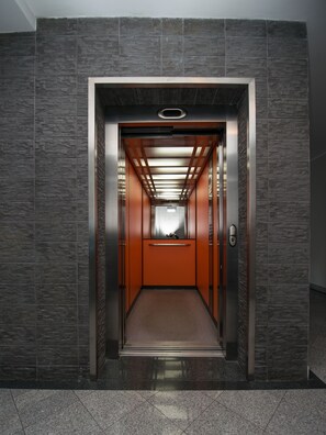 An elevator with a stone-textured wall, a metallic interior, and a handrail. - Fresh Apart Marina (Bydgoszcz)