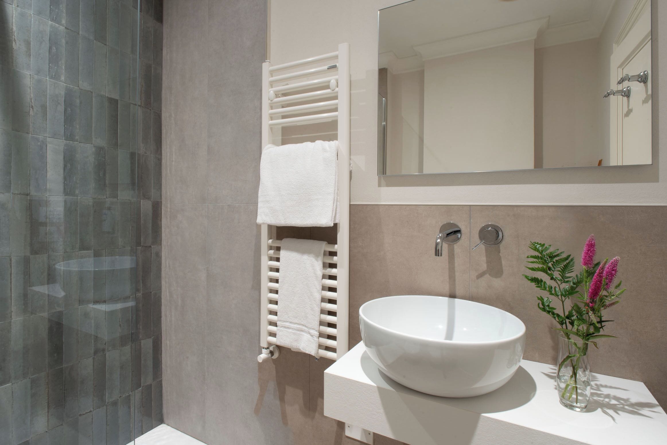 A modern bathroom with a large white sink, a mirror, and a towel rack.