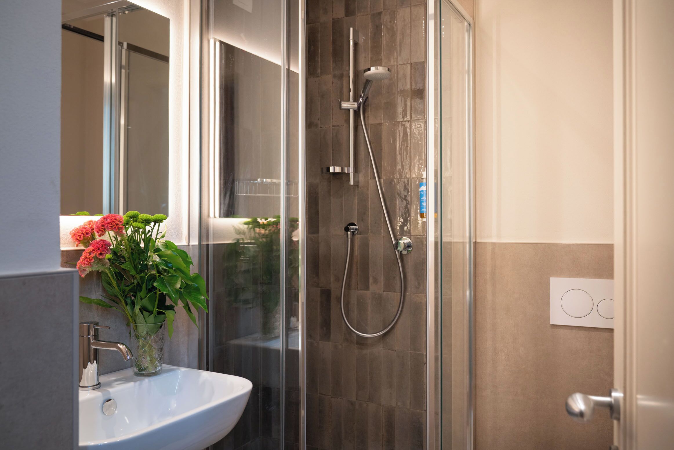 A modern bathroom with a glass shower enclosure, a white sink, and a vase with flowers.