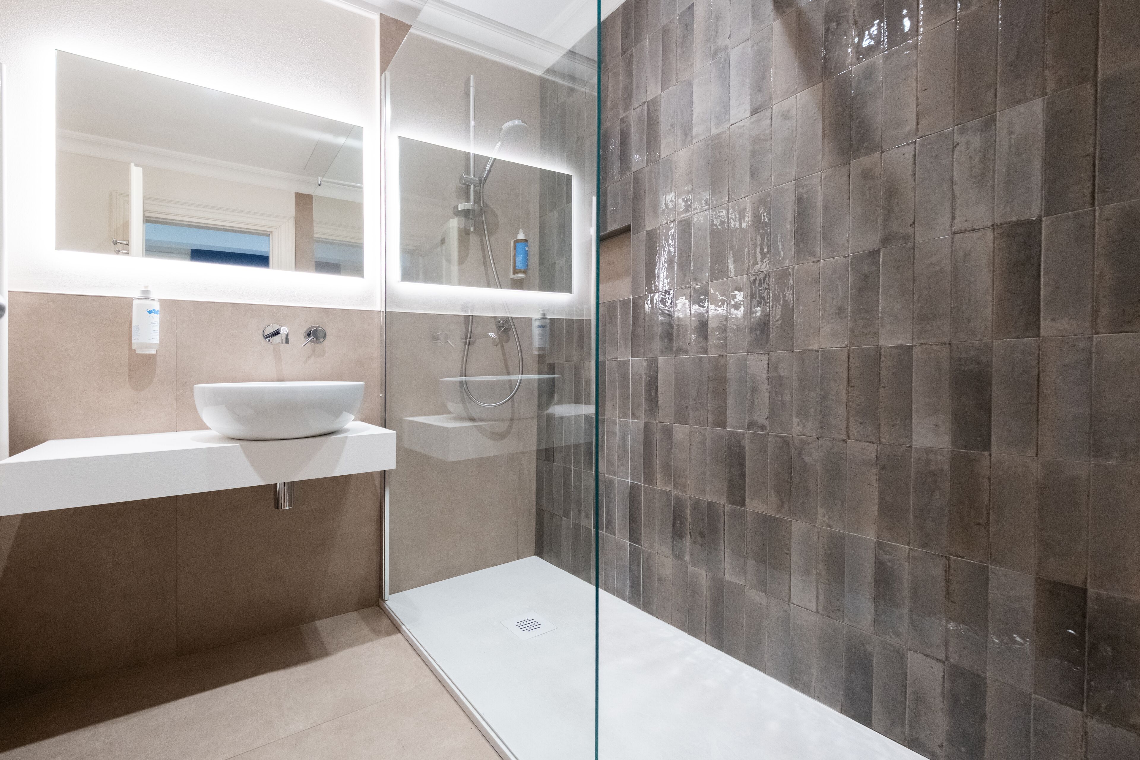Een moderne badkamer met een wit wastafelmeubel, een douchecabine van glas en een betegelde wand.