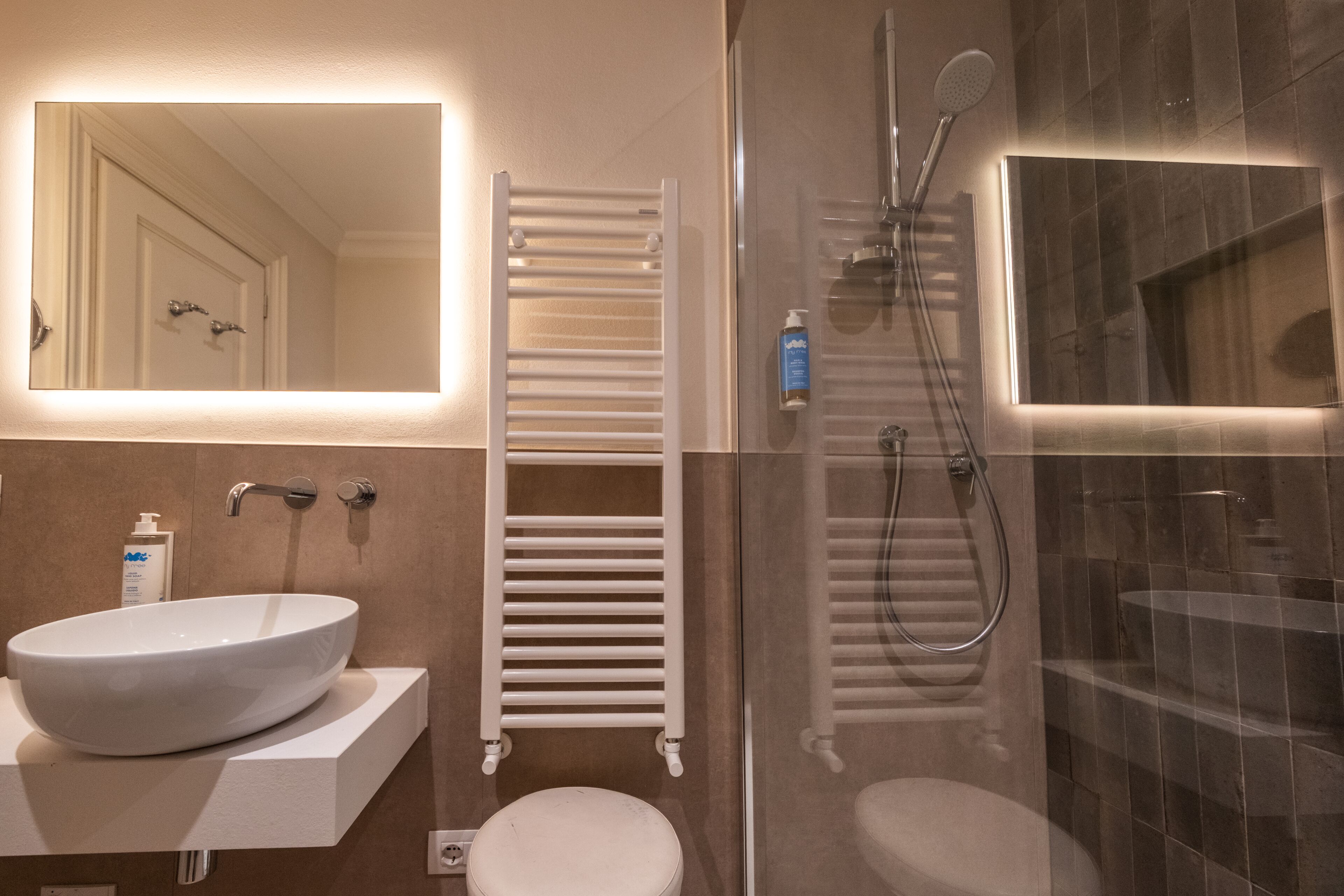 Un baño con lavamanos blanco, inodoro, cabina de ducha de vidrio y un perchero para toallas.