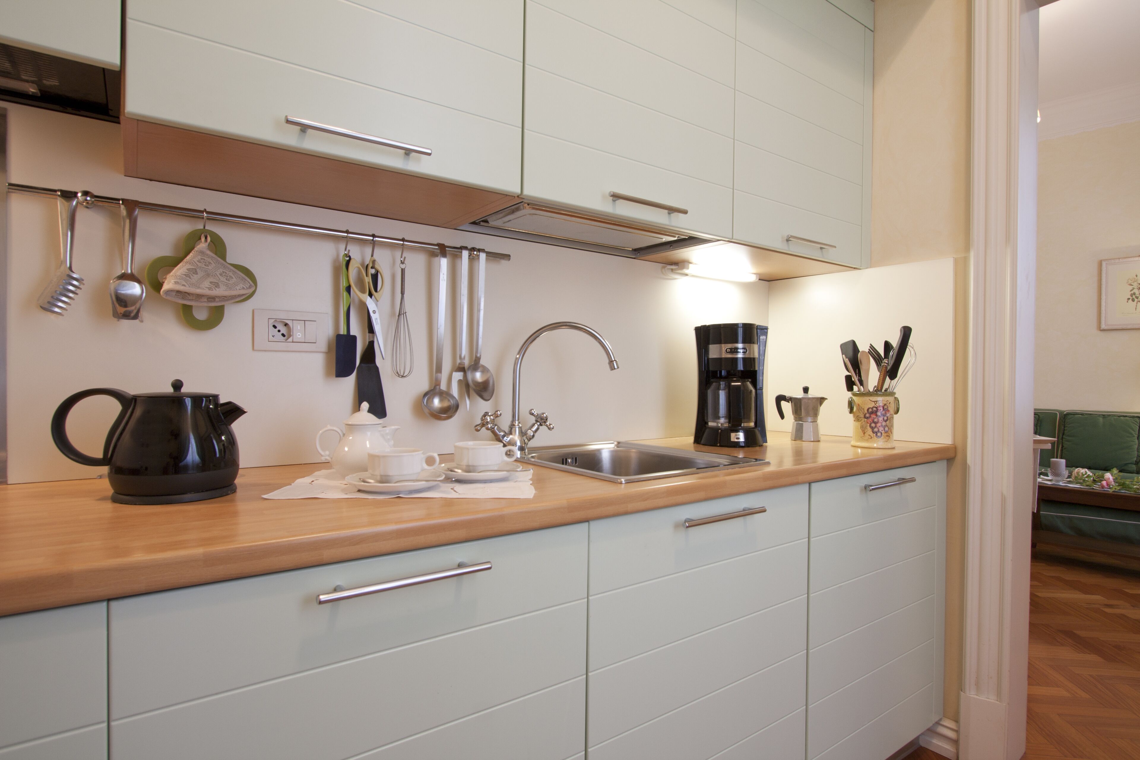 Une cuisine avec des meubles blancs, un plan de travail en bois, une machine à café et divers ustensiles accrochés au mur.