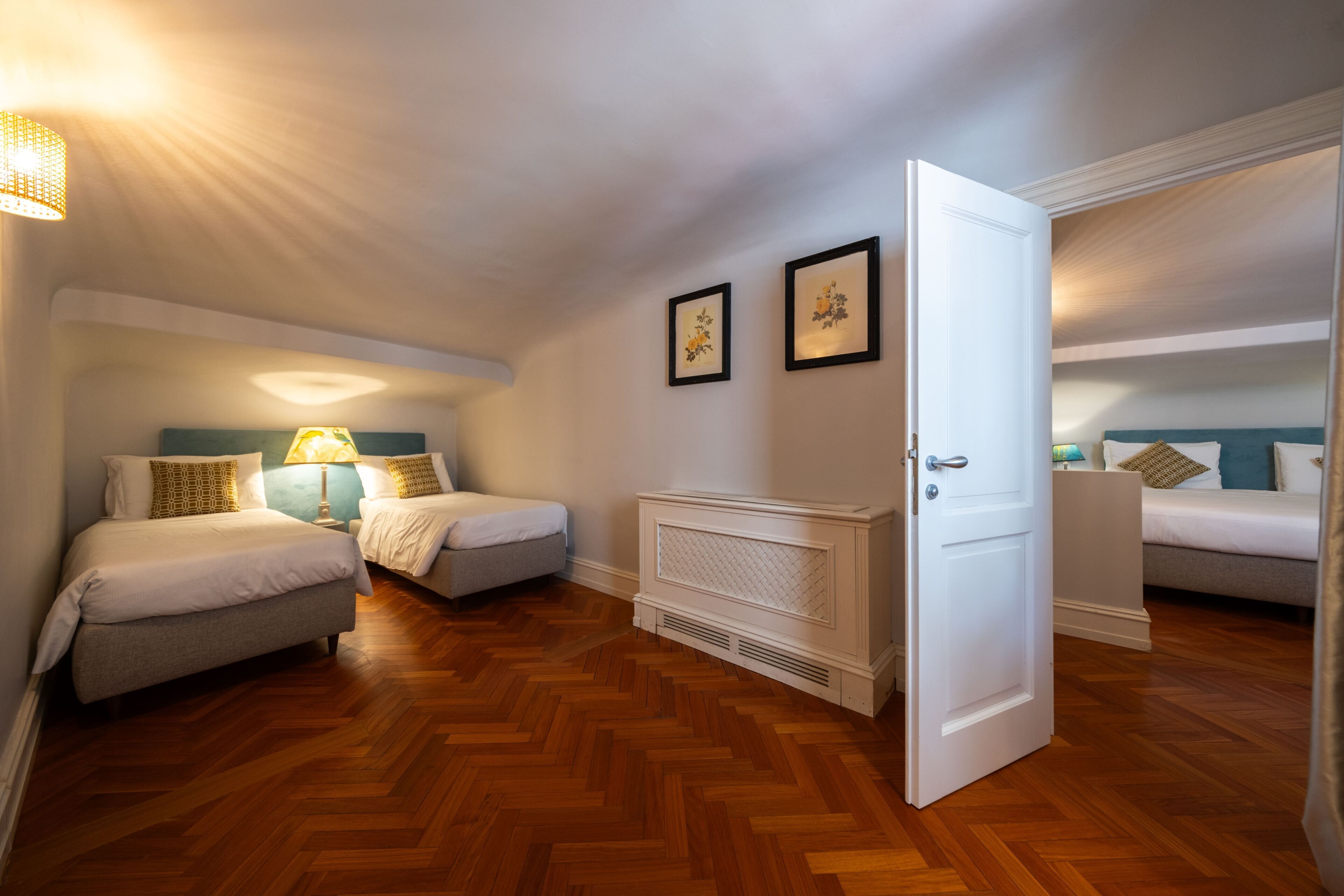 A hotel room with two beds, a radiator, and a door leading to another room.