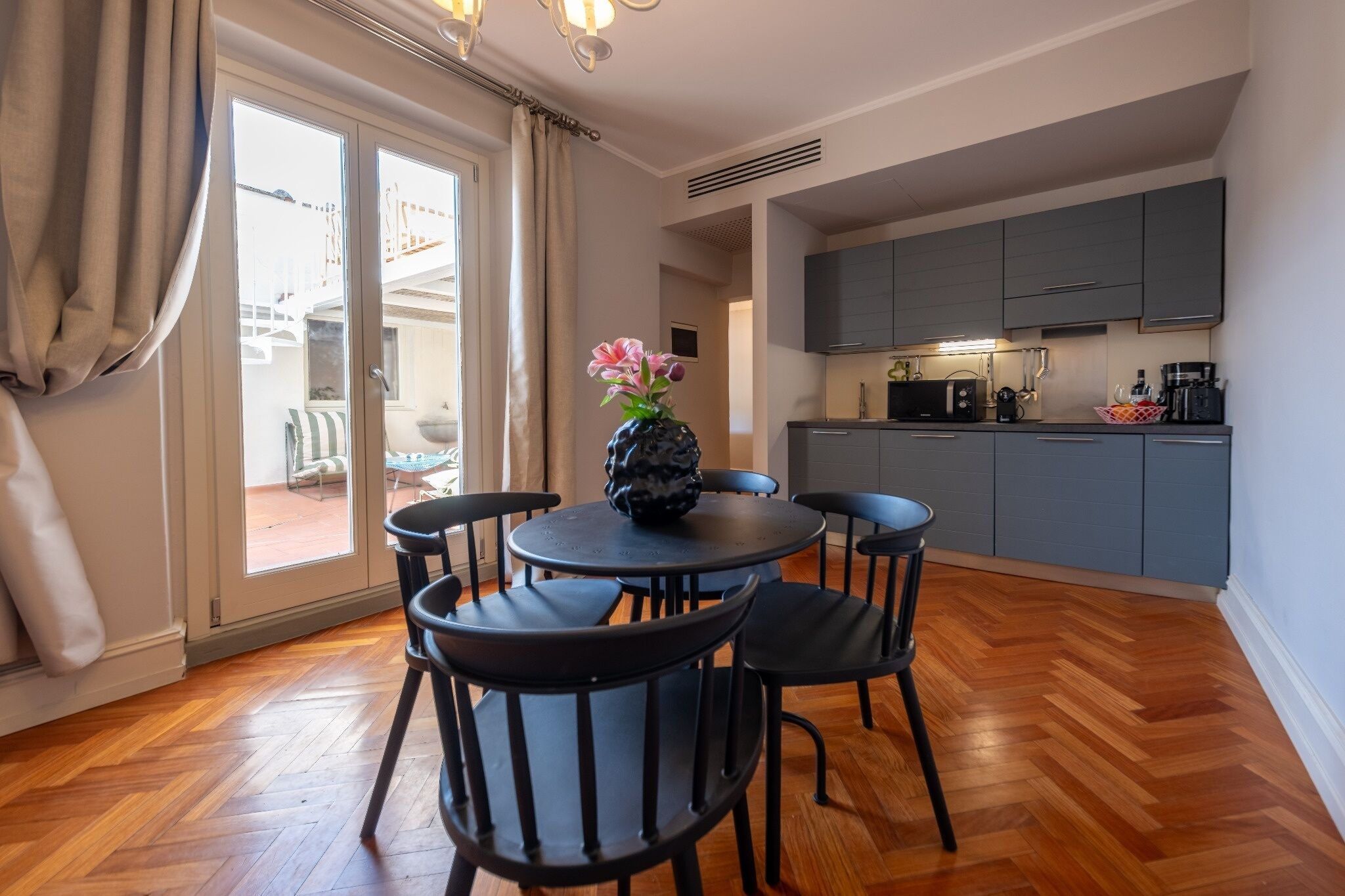 Un coin repas avec une table ronde, quatre chaises, un vase de fleurs et une cuisine en arrière-plan.