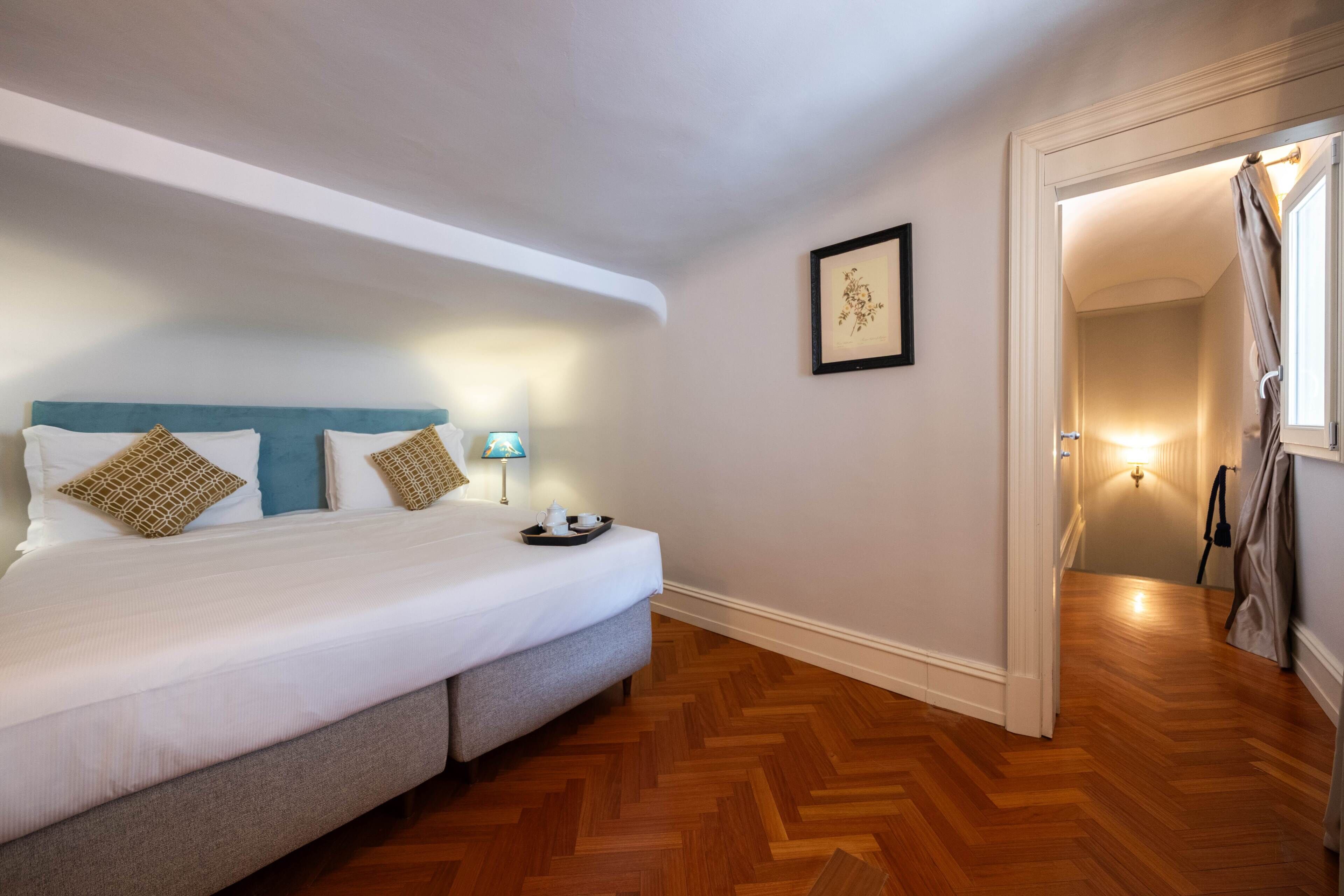 A bedroom with a bed, a nightstand, a lamp, a framed picture on the wall, and a wooden floor.