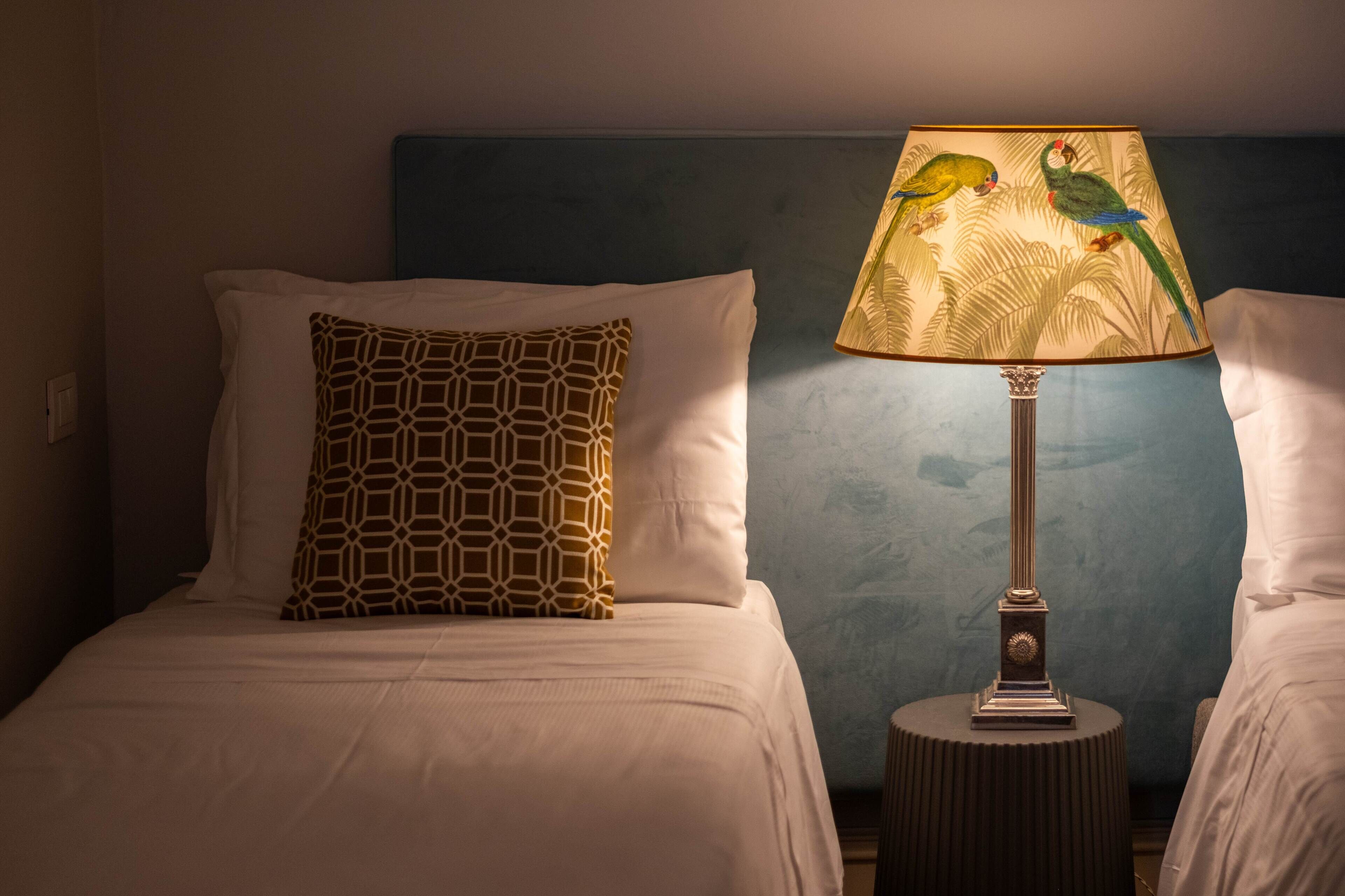 A hotel room with a bed, a patterned pillow, a lamp with a bird design, and a nightstand.