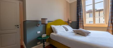 A hotel room with a bed, a nightstand, a window with curtains, and a door.