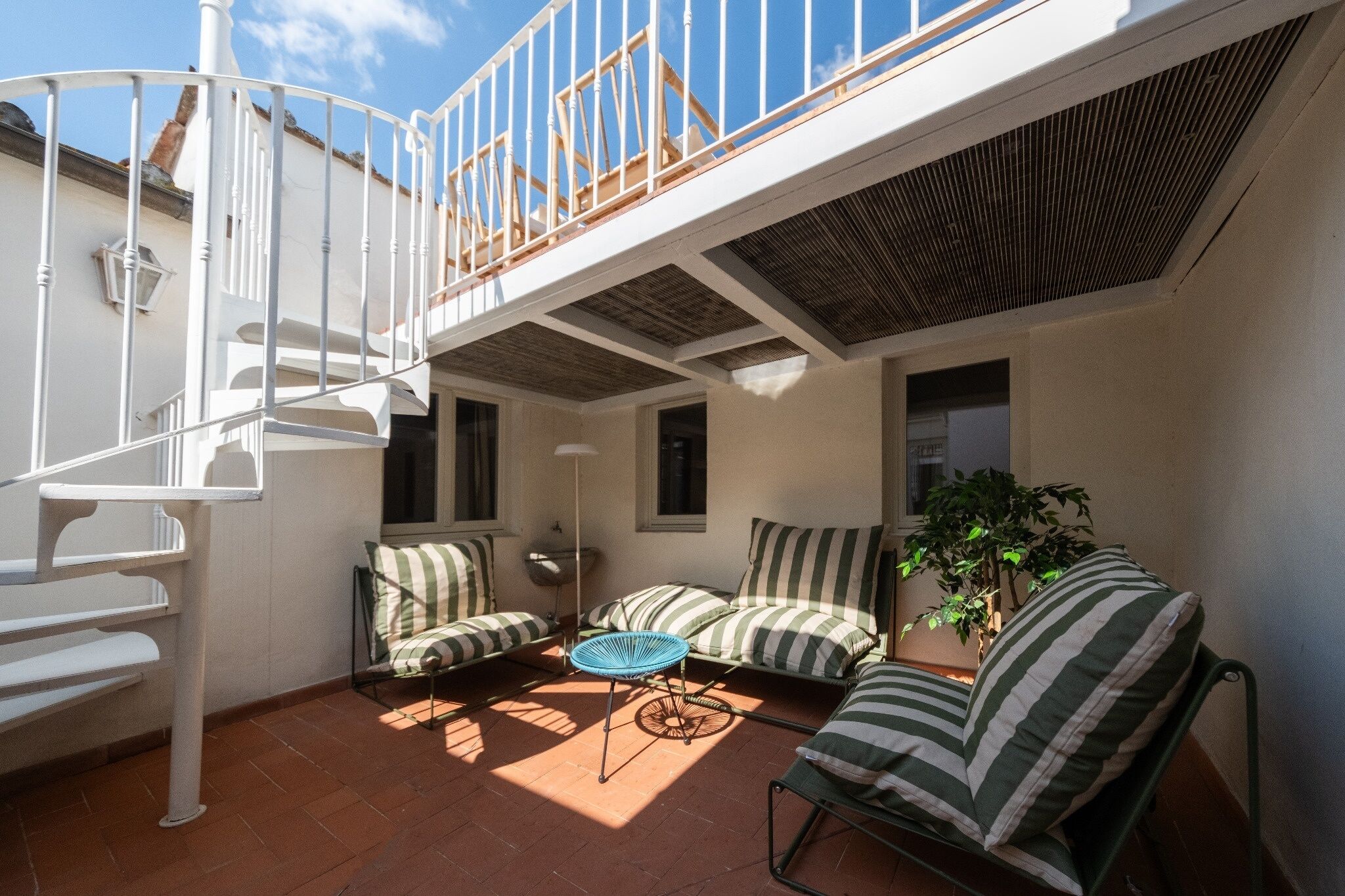 A sunlit patio with a spiral staircase, striped cushions, and a potted plant.