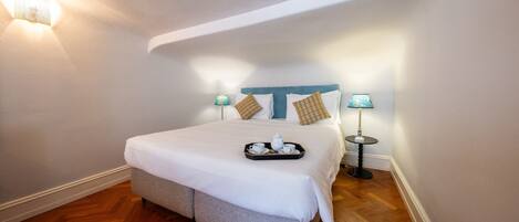 A neatly made bed with a tray of tea and cups, two bedside lamps, and a wooden floor.