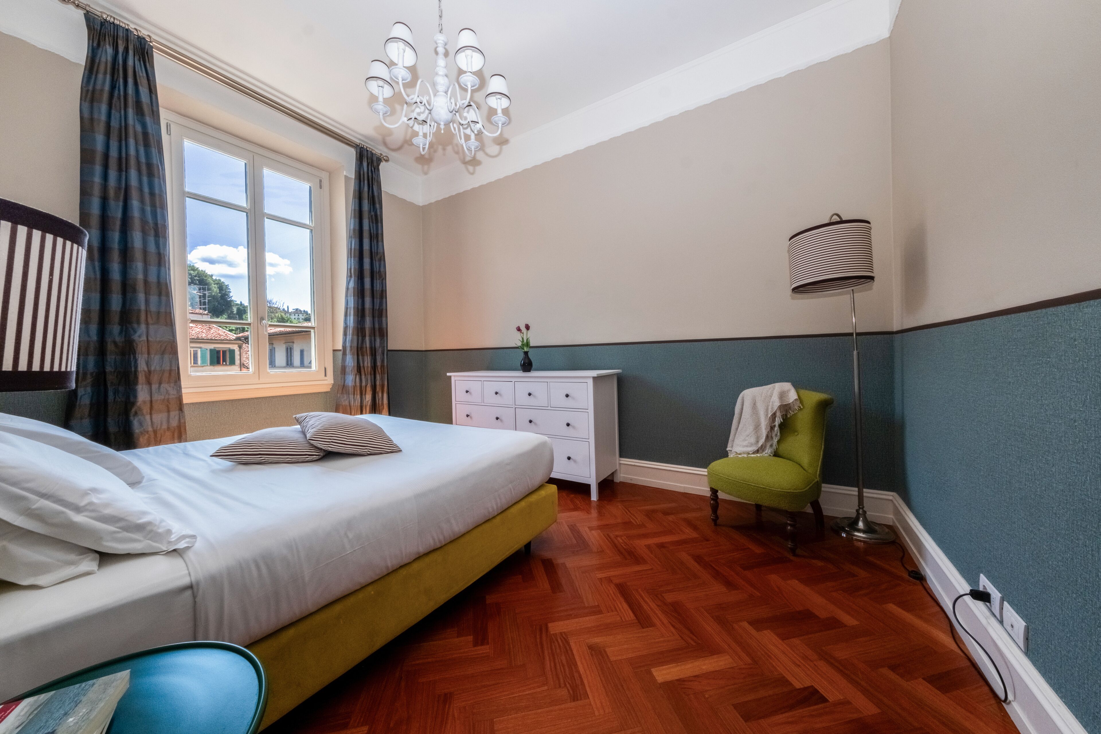 A bedroom with a bed, a dresser, a chair, and a floor lamp.