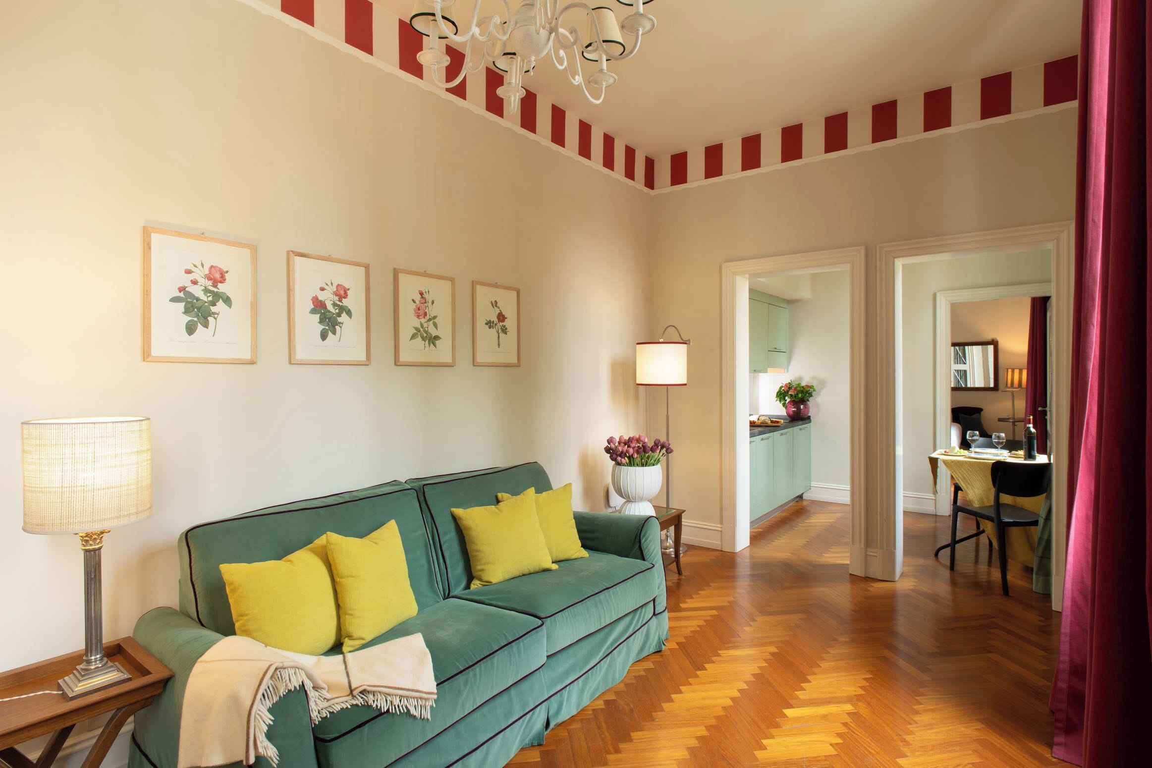 Un salon avec un canapé vert, des coussins jaunes, une lampe et des œuvres d’art florales encadrées accrochées au mur.