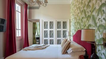 Habitación de hotel con una cama grande, un escritorio y una silla. Hay una ventana con cortinas rojas y una puerta con paneles de vidrio.