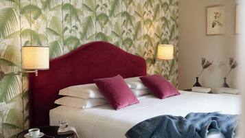 Habitación de hotel con una cama grande, dos almohadas, una mesita de noche con una lámpara, una pequeña mesa con una taza y un vaso, y una pared con diseño de hojas de palma.
