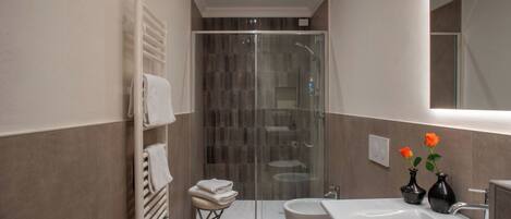 A modern bathroom with a glass shower enclosure, a large sink, and two vases with flowers.