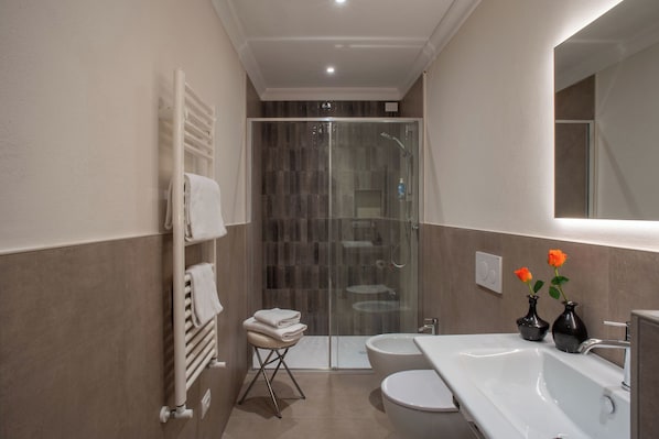 Un baño moderno con mampara de cristal, un lavamanos amplio y dos jarrones con flores.