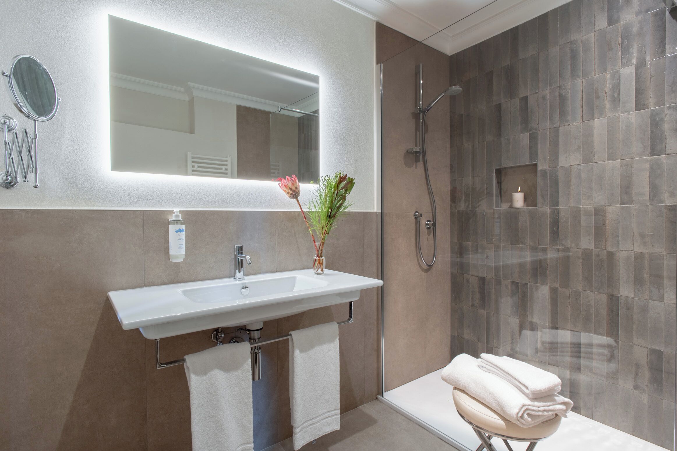 Ein modernes Badezimmer mit großem Spiegel, Waschbecken, Dusche und Handtuchhalter.