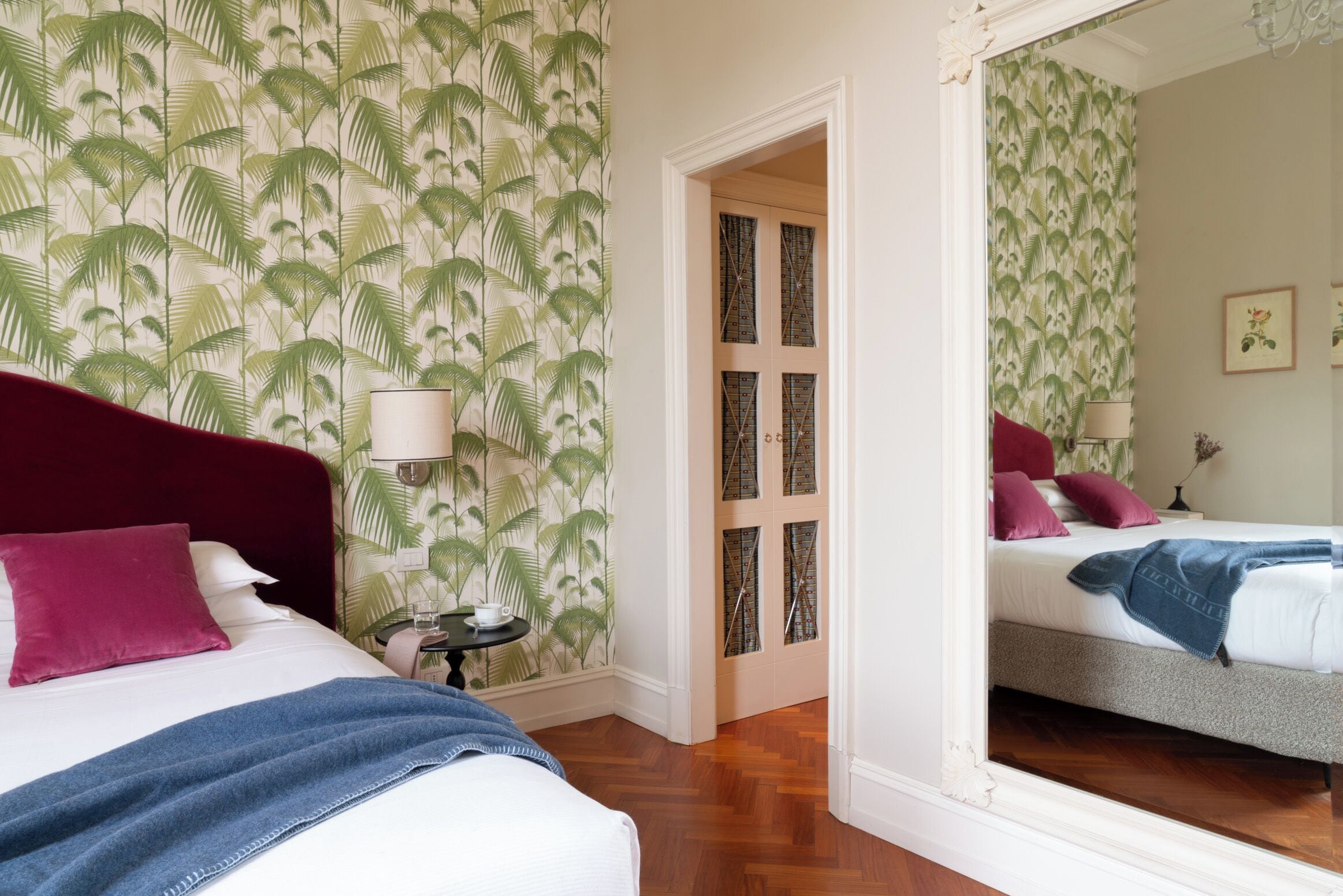 Ein Schlafzimmer mit einem Bett, einem Nachttisch, einem Spiegel und einer Tür zu einem anderen Raum.