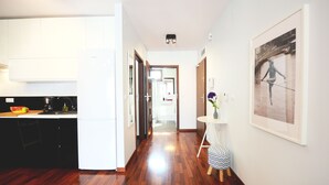 Una cocina moderna con piso de madera, un comedor con una mesa pequeña y sillas, y un pasillo que lleva a un baño.