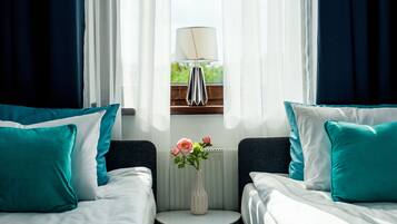 A hotel room with two beds, a small table with a vase of flowers, and a lamp on a shelf.