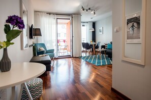 A modern living room with a wooden floor, a dining area with a table and chairs, and a balcony with a view. - Fresh Apart Stawowa (Bydgoszcz)